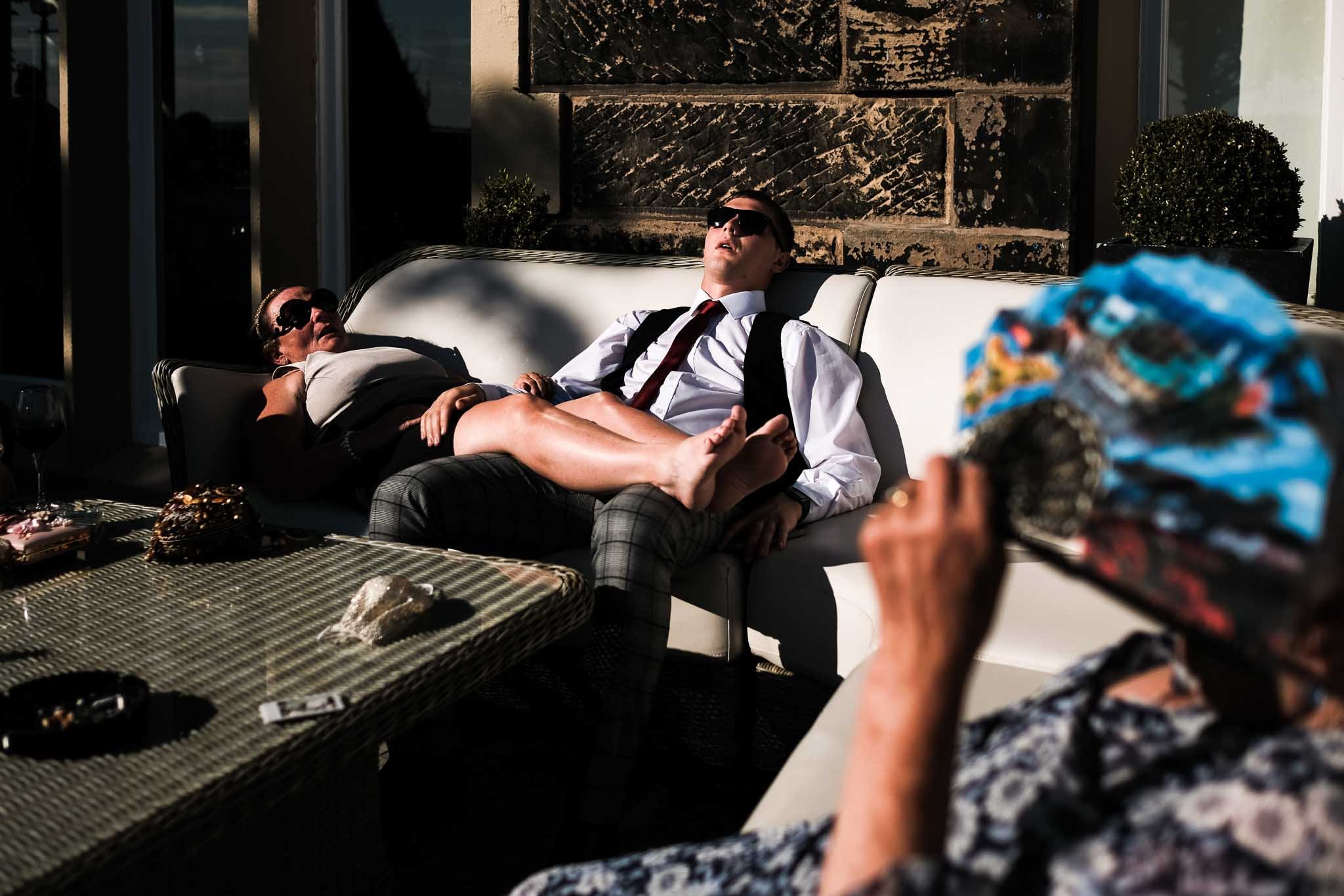 a natural wedding photograph of guests relaxing in the sun after the wedding breakfast at West Tower Lancashire wedding venue.